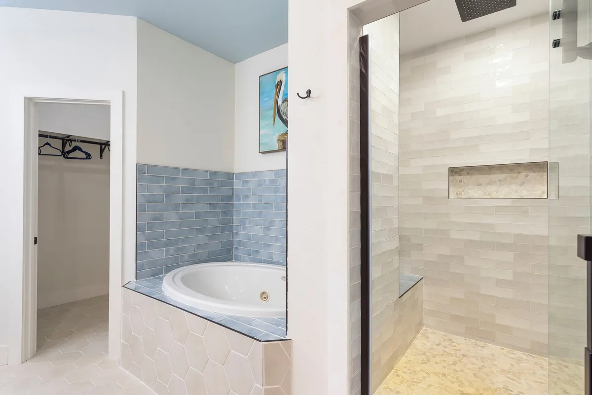 A tranquil spa-inspired bathroom with a jacuzzi tub, shower area, blue tiled walls, and calming ocean-themed artwork. The space feels luxurious and calming, ideal for unwinding after a day of adventure.