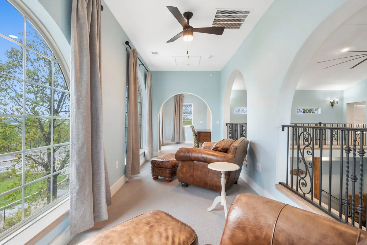 A light-filled room with large arched windows, leather seating, and soft curtains creates a cozy nook ideal for reading or quiet moments. The inviting atmosphere highlights the flexibility of the home for private retreats and peaceful downtime.