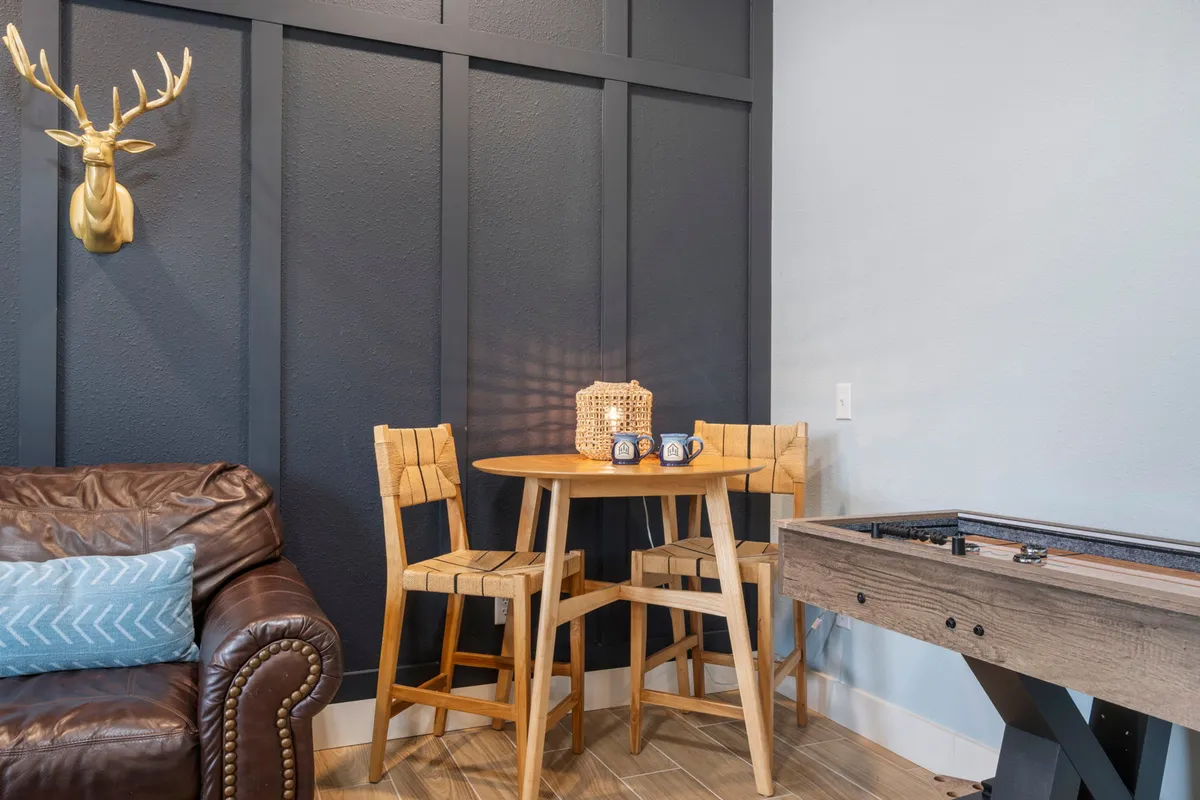 A casual interior lounge with wooden chairs, a chocolate brown leather sofa, antler wall decor, and a foosball table. The space invites casual conversations, drinks, and friendly games after a day exploring nearby attractions.
