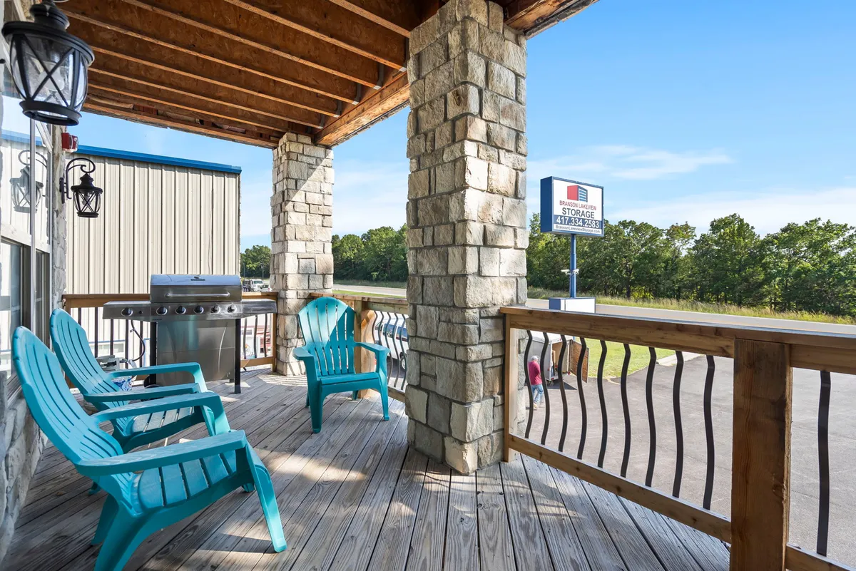 An inviting outdoor deck featuring wooden construction, stone columns, comfortable seating, and a grill setup. The scene suggests a relaxed social gathering area with views toward the natural surroundings, perfect for enjoying the outdoors.