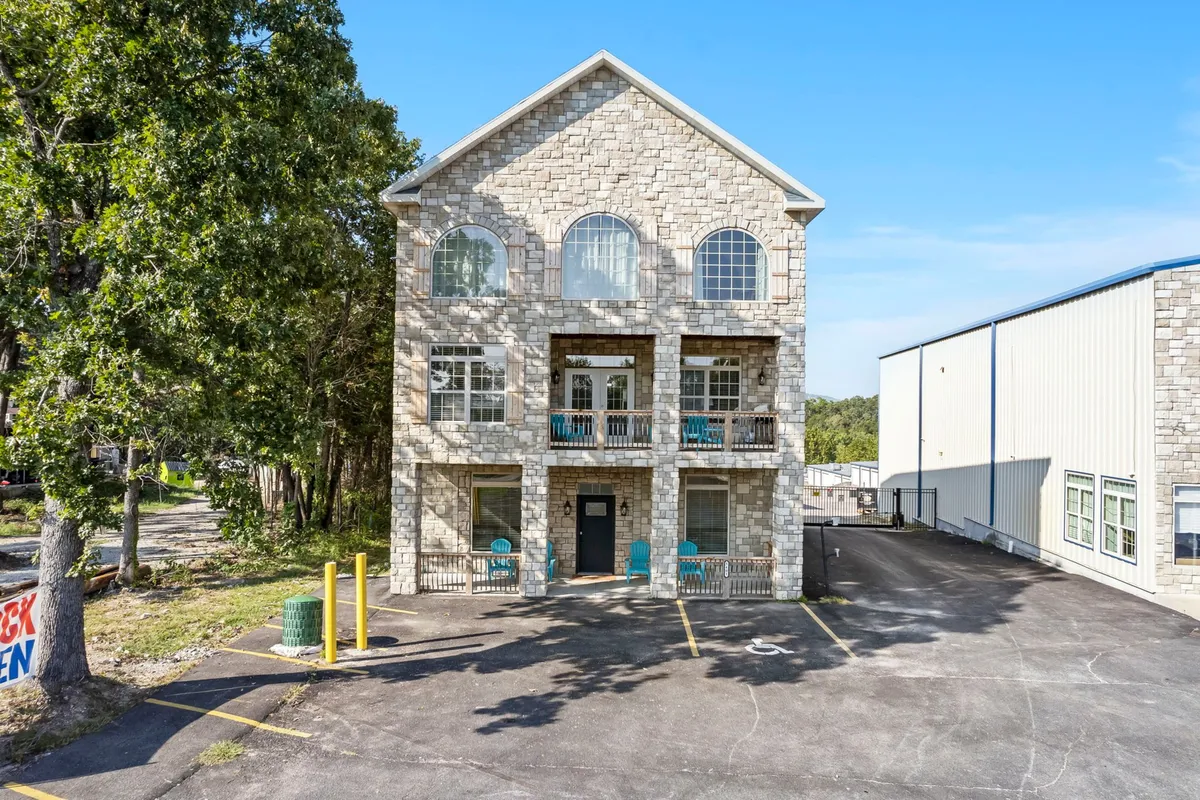 An exterior view of the home showing a stone facade, large arched windows, balconies with outdoor seating, and a welcoming front door. There is ample space by the driveway, suitable for parking vehicles or even a boat, and the atmosphere is peaceful and inviting—ideal for pet-friendly stays and outdoor adventures.