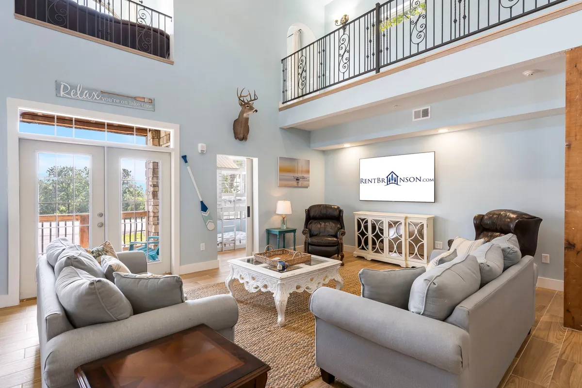 A spacious and inviting living area featuring plush sofa seating, a stylish coffee table, and a large television. Sunlight pours in through the windows, offering a glimpse of the scenic outdoors and setting the stage for cozy family gatherings, relaxing movie nights, and shared laughter.