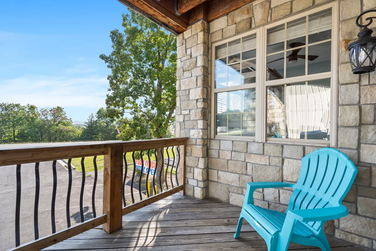 This exterior image showcases a tranquil porch area with a stone wall, wooden railing, and a bright blue chair surrounded by lush green trees. The natural setting invites relaxation and offers a direct connection to the outdoor environment, suggesting a peaceful spot to unwind after a day of lakeside adventure.
