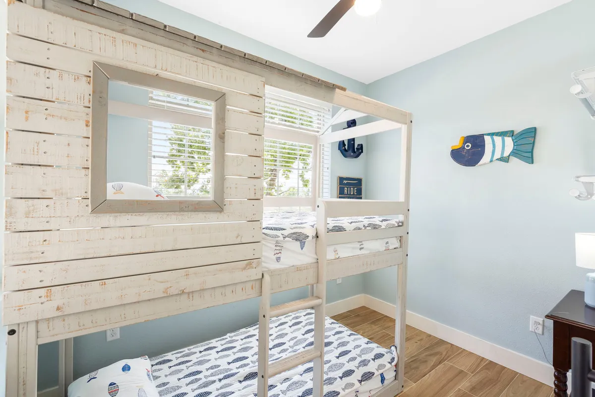 A cheerful bunk room with a nautical theme, including a twin-over-twin bunk bed, colorful fish wall decor, and ample natural light from windows. The playful decor invites both kids and adults for a fun and memorable sleepover experience.