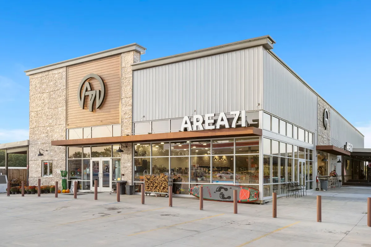 A modern and stylish exterior shot of AREA71, with a prominent sign, expansive glass windows, and contemporary architecture. The vibe is lively, hinting at entertainment, socializing, and food offerings nearby.