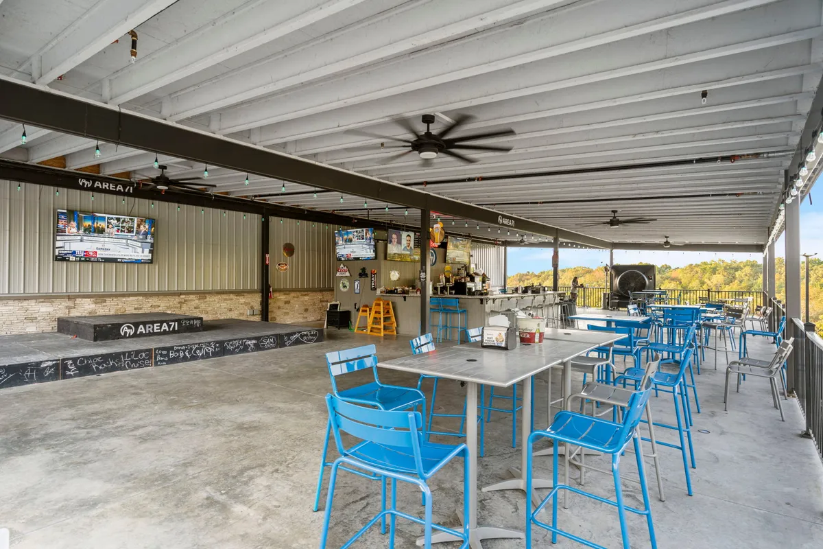 An inviting outdoor bar area featuring tables and chairs, multiple televisions, and a dedicated stage area. The scene is set for socializing, dining, and enjoying live performances, with a lively yet relaxed atmosphere.