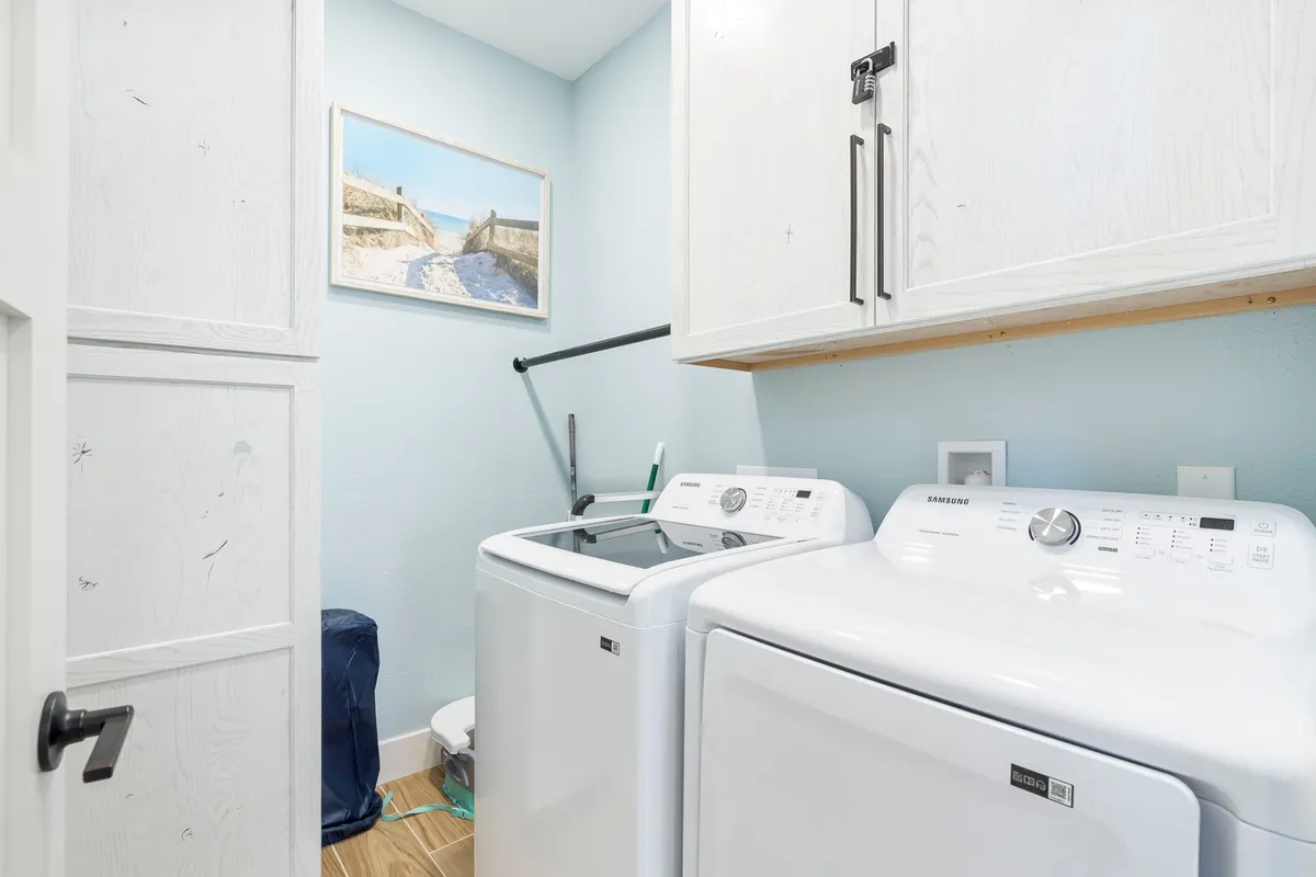 A well-organized laundry space with a washing machine, dryer, wall art, and storage cabinets, creating a tidy and efficient place for handling laundry needs during a stay. The mood is efficient and organized, aligning with the idea of longer or more active visits.